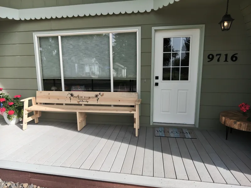 The front porch with the Pickin&rsquo; Daisies bench, a welcome mat and geraniums