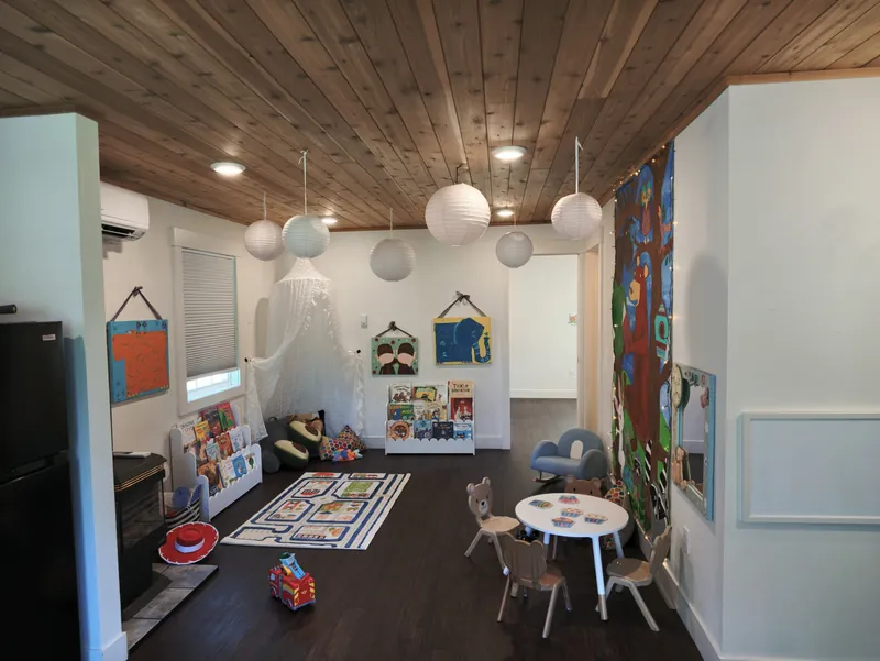 The classroom looking through to the kitchen, with low shelves and a play rug